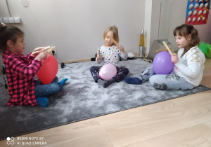 Dziewczynki grają na balonie drewnianymi pałkami.